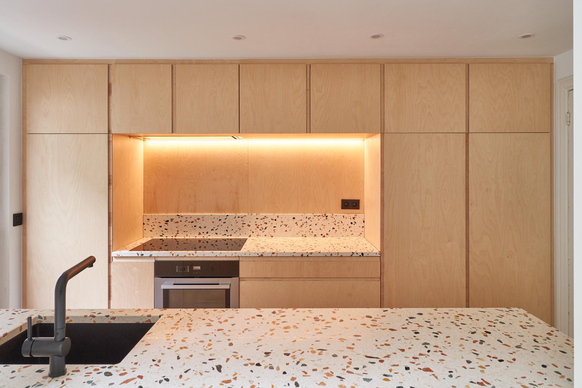 cuisine, lavabo noir, plan de travail terrazzo, armoires en bois multiplex, éclairage niche table de cuisson